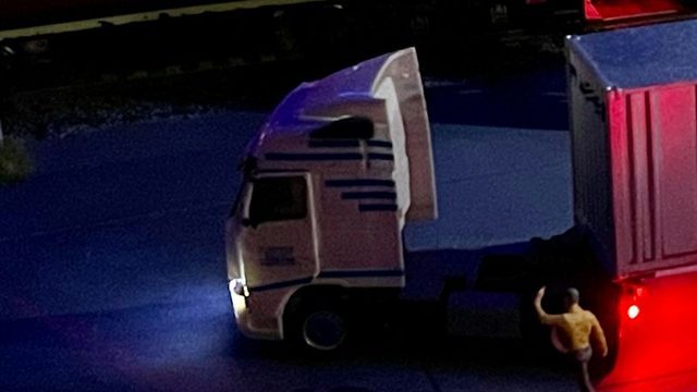 A tractor unit standing at its trailer on dark tarmac at night, one red marker light burning.